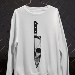 May include: White sweatshirt with a black and white graphic of a skull inside a knife.
