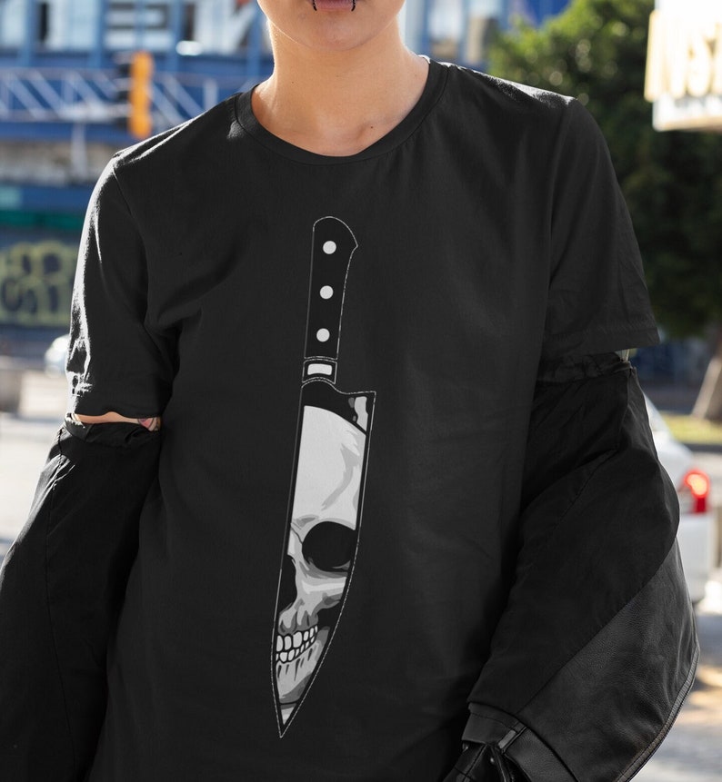 May include: Black t-shirt with a graphic of a white skull inside a kitchen knife.