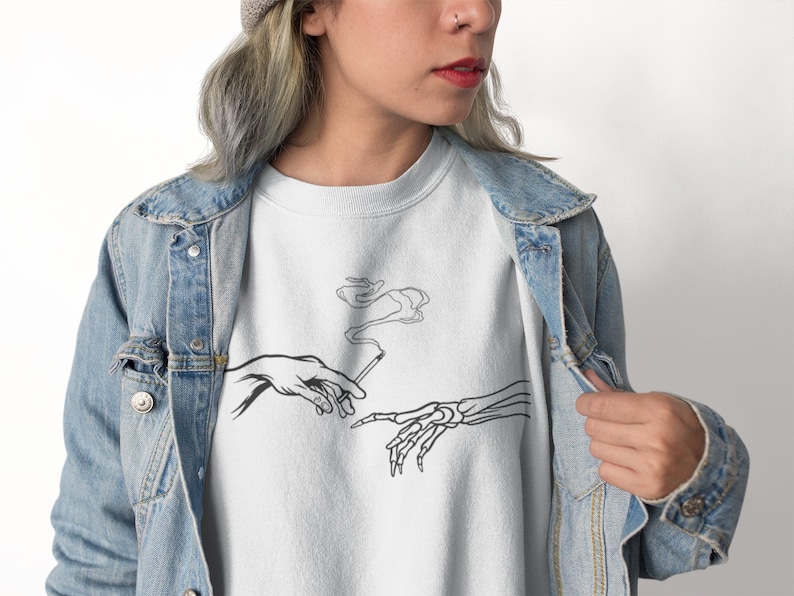 May include: A white sweatshirt with a black and white graphic of two hands reaching towards each other, one hand holding a cigarette with smoke rising from it. The graphic is a parody of Michelangelo's The Creation of Adam.