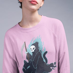 K&ouml;nnte beinhalten: Ein rosa Sweatshirt mit einem Grafikdruck des Sensenmanns, der auf einer schwarzen Katze reitet. Der Sensenmann h&auml;lt eine Sense und ist von blauen Flammen umgeben.