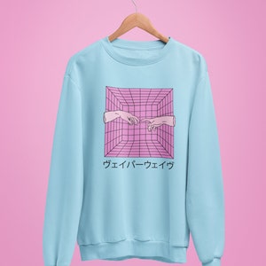 May include: Light blue sweatshirt with a pink and black geometric design featuring two hands reaching towards each other. Japanese text is below the graphic. The sweatshirt is hanging on a wooden hanger.