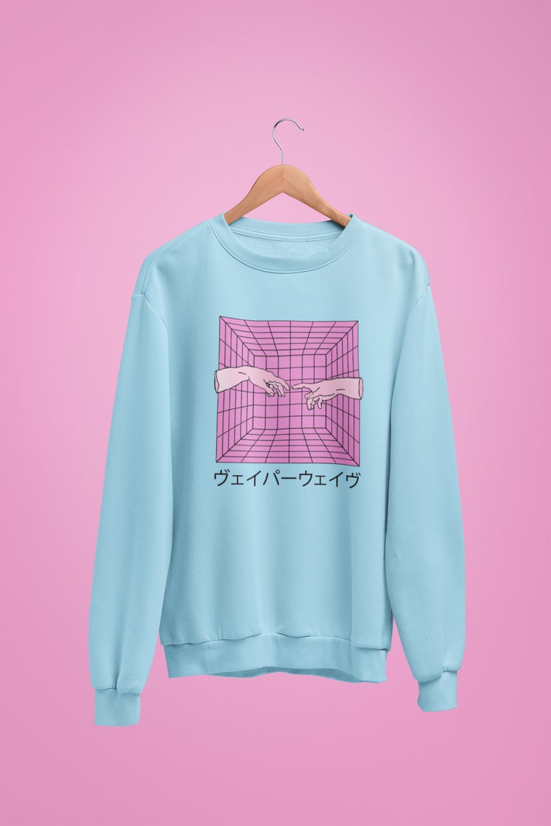May include: Light blue sweatshirt with a pink and black geometric design featuring two hands reaching towards each other. Japanese text is below the graphic. The sweatshirt is hanging on a wooden hanger.