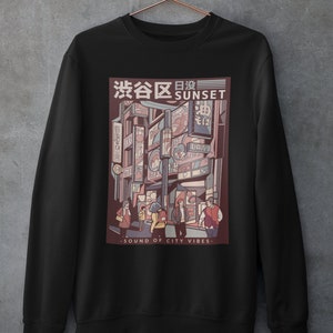 May include: Black sweatshirt with a graphic print of a city street scene at sunset. The graphic features a Japanese text that says "渋谷区日没" which translates to "Shibuya Sunset" and the text "SOUND OF CITY VIBES".