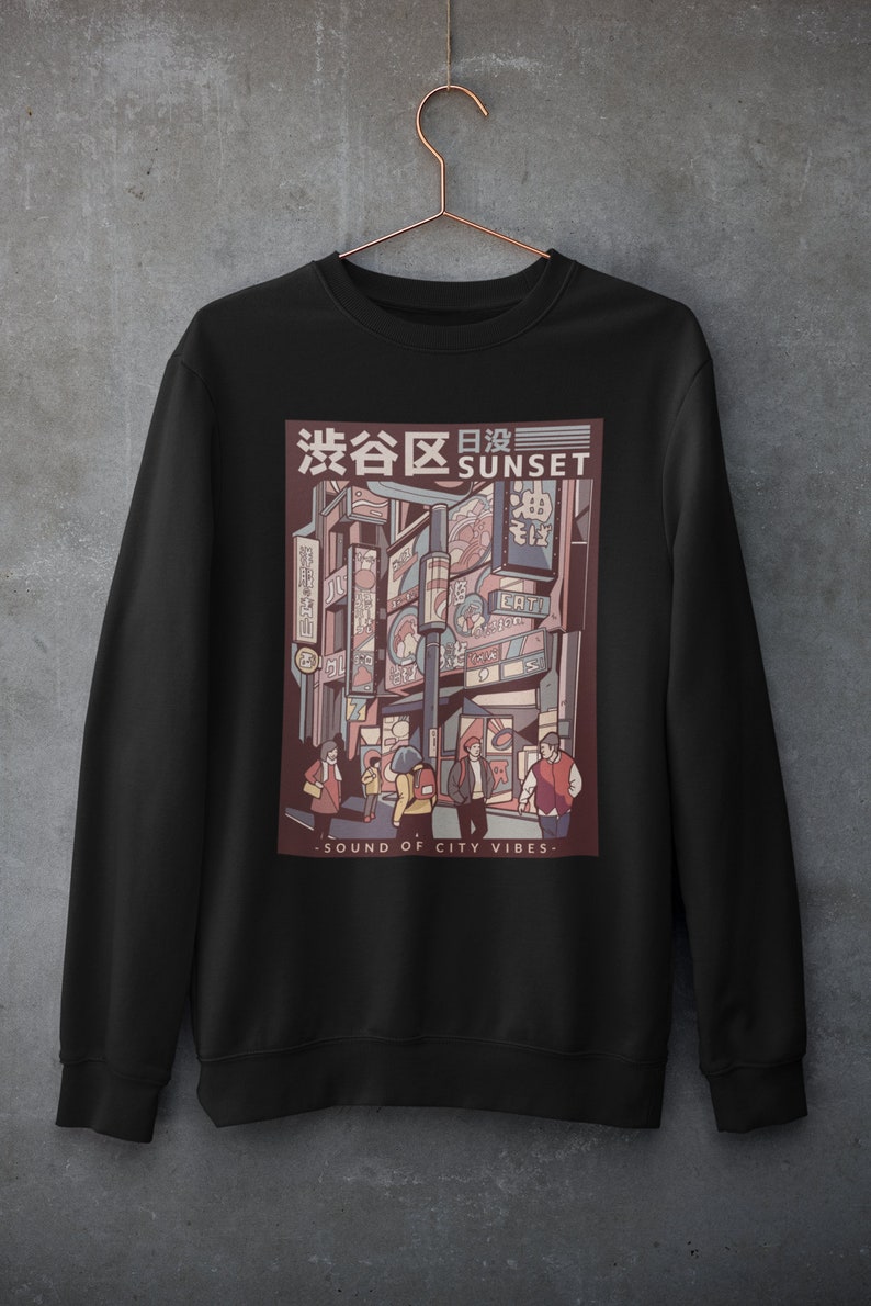 May include: Black sweatshirt with a graphic print of a city street scene at sunset. The graphic features a Japanese text that says "渋谷区日没" which translates to "Shibuya Sunset" and the text "SOUND OF CITY VIBES".