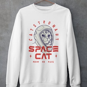 May include: White sweatshirt with a graphic of a cat wearing an astronaut helmet. The text reads "Catstronaut Space Cat Meow On Mars".