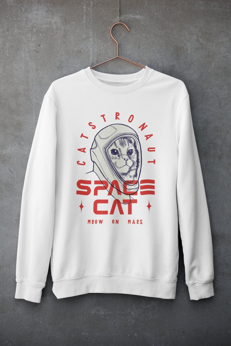 May include: White sweatshirt with a graphic of a cat wearing an astronaut helmet. The text reads "Catstronaut Space Cat Meow On Mars".