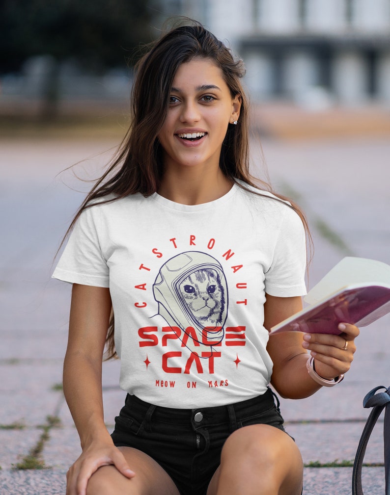 May include: White t-shirt with a graphic of a cat wearing an astronaut helmet. The graphic says "Cats-tronaut Space Cat Meow on Mars".