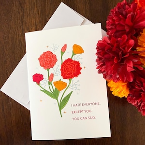 May include: A white greeting card with a floral illustration of red and orange flowers, green stems, and small star accents. The text on the card reads: I HATE EVERYONE. EXCEPT YOU. YOU CAN STAY. The card is paired with a white envelope.