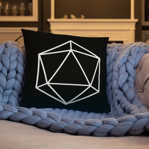 Puede incluir: Una almohada negra con un diseño geométrico blanco que se asemeja a un dado de 20 caras.
