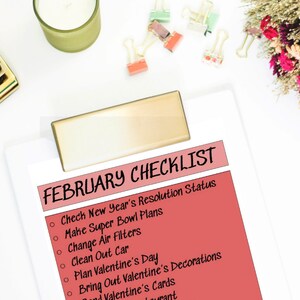 Könnte beinhalten: Eine rosa Checkliste auf einem weißen Clipboard mit dem Titel "FEBRUARY CHECKLIST". Die Checkliste enthält Punkte wie "Neujahrsvorsätze überprüfen", "Super Bowl Pläne machen", "Luftfilter wechseln", "Auto putzen", "Valentinstag planen", "Valentinstagsdekorationen auspacken" und "Valentinstagskarten verschicken".