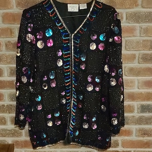 May include: Black sequined jacket with colorful iridescent sequins and a gold trim. The jacket has a V-neck and a zipper closure. The sequins are arranged in a grid pattern, creating a dazzling effect. The jacket is a vintage piece.
