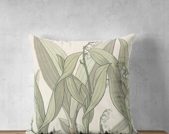 Puede incluir: Una almohada blanca con un patrón floral verde con flores y hojas de lirio de los valles.