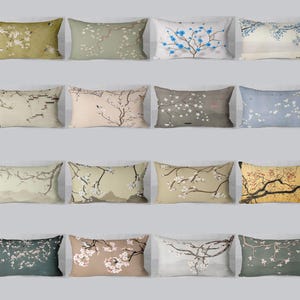 Può includere: Una collezione di cuscini rettangolari con vari disegni floreali e paesaggistici. I cuscini presentano una gamma di colori, tra cui verde oliva, beige e blu, con illustrazioni dettagliate di fiori di ciliegio e rami.