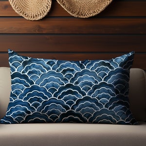 May include: A blue and white patterned throw pillow with a geometric design. The pillow is on a light gray couch in front of a wood wall.