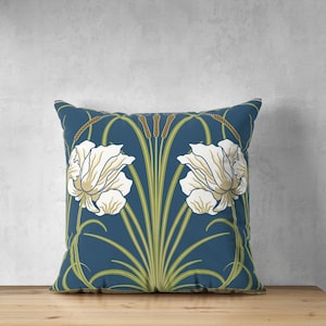 May include: A blue throw pillow with a white floral pattern. The pillow features stylized white flowers with green leaves and brown stems on a dark blue background.
