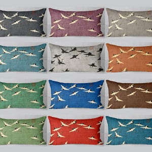 Peut inclure: Coussins rectangulaires de différentes couleurs, dont le gris, le violet, le bleu sarcelle et le marron. Chaque coussin présente un motif répété de grues en vol en blanc et noir, créant un design artistique classique.