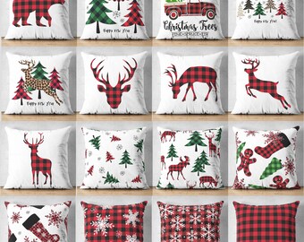 May include: A collection of sixteen square throw pillows featuring various holiday-themed designs including red and black buffalo plaid bears, deer, snowflakes, Christmas trees, stockings, gingerbread men, and a truck with the text Farm Fresh Christmas Trees.