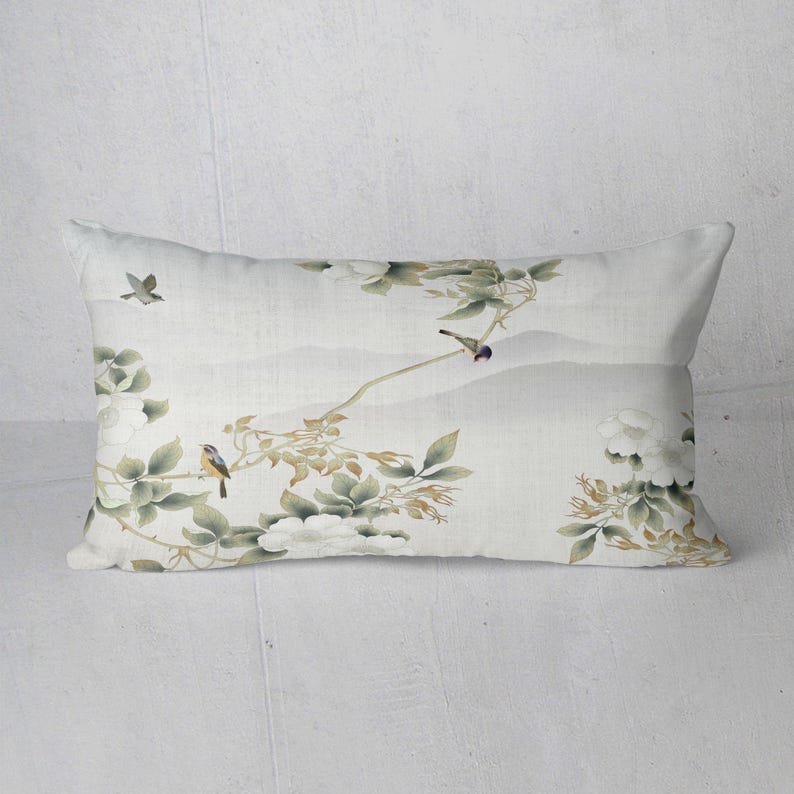 May include: Rectangular decorative pillow with a serene, watercolor-style design. The pillow features a light background with a landscape of mountains and branches with birds and white flowers. The color palette includes shades of green, white, and gray.