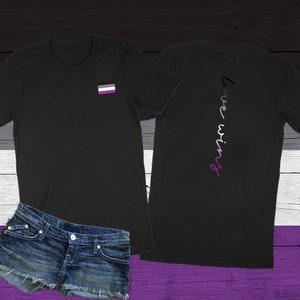 May include: Black t-shirt with a small asexual pride flag on the left chest and the words "Love wins" written vertically down the back in a gradient of purple, white, and black.