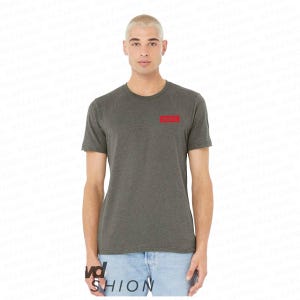 Op de afbeelding: Een donkergrijs T-shirt met ronde hals en een klein rood rechthoekig ontwerp op de linkerbovenborst. Het shirt heeft korte mouwen en is gemaakt van een zacht materiaal. Het model draagt een lichtblauwe jeans.
