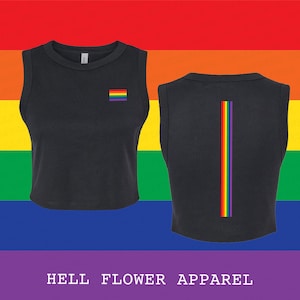May include: Black crop top with a rainbow flag on the front and a vertical rainbow stripe on the back. The top is sleeveless and has a crew neck. The background is a rainbow gradient. Text at the bottom reads "HELL FLOWER APPAREL".
