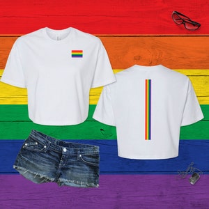Pu&ograve; includere: Una t-shirt bianca corta con una piccola bandiera arcobaleno sul petto sinistro e un design a striscia verticale arcobaleno centrato sul retro. Il set include un paio di pantaloncini in denim blu con orlo sfrangiato e una piastrina d'argento.