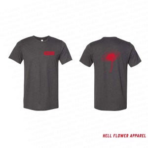 Op de afbeelding: Twee donkergrijze t-shirts met rode details. E&eacute;n shirt heeft een rood rechthoek op de borst, de andere een rood paardenbloemontwerp op de rug. De tekst "HELL FLOWER APPAREL" staat onderaan de afbeelding.