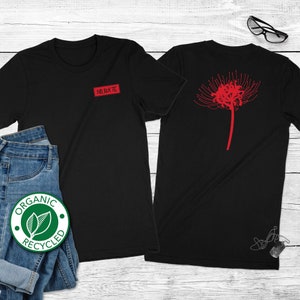 Op de afbeelding: Zwarte t-shirts met een rood bloemmotief op de achterkant en een kleine rode patch met Japanse tekst op de voorkant. De shirts worden getoond met een blauwe jeans en een groen-witte "Organic Recycled" sticker.