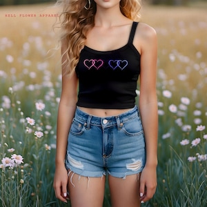 May include: A black tank top with a graphic of three interlocking hearts in pink, blue, and purple. The tank top is cropped and has thin straps.