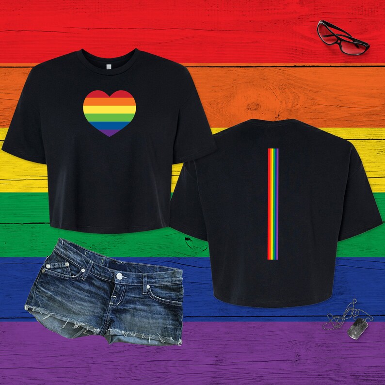 Pu&ograve; includere: Una t-shirt nera corta con un cuore color arcobaleno sul davanti e una striscia verticale arcobaleno sul retro, esposta insieme a un paio di pantaloncini di jeans blu, occhiali con montatura nera e una collana con piastrina argentata.