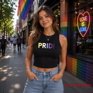 May include: Black tank top with the word "PRIDE" in yellow, white, and purple. The tank top is worn with blue jeans. A rainbow flag hangs in the background. The image also includes a neon sign that says "LOVE IS LOVE".