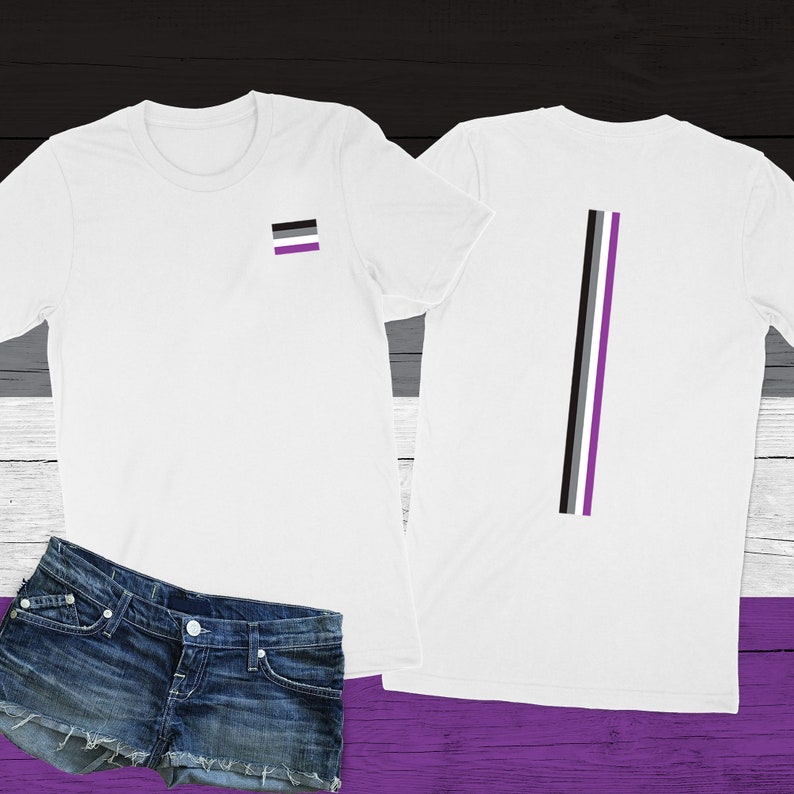 May include: White t-shirt with a black, gray, and purple stripe on the back and a small black, gray, and purple flag on the front. The shirt is shown on a wooden background.
