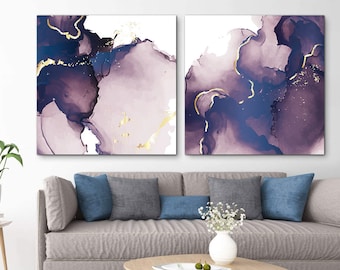 Puede incluir: Dos pinturas abstractas con remolinos de acuarela de color púrpura y azul y detalles dorados. Las pinturas están colgadas en una pared sobre un sofá gris con almohadas azules.