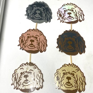 May include: Six different dog head cake toppers. The toppers are made of paper and have a glittery finish. The dogs are all different colours, including black, brown, gold, and silver.