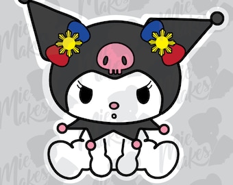 Puede incluir: Un personaje de dibujos animados en blanco y negro con una nariz rosa y una calavera en la frente. El personaje lleva un gorro de bufón negro y azul con un sol amarillo y detalles de corazón rojo. El personaje está sentado con las piernas cruzadas.