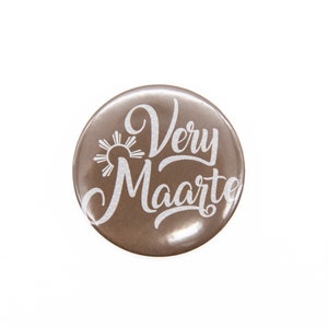 May include: A brown round button with a white sun and the text "Very Maarte" in a white cursive font.