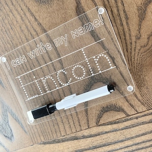 May include: A clear plastic dry-erase board with the text "I can write my name!" and the name "Lincoln" written in dotted lines. A white dry-erase marker with a black cap is included.