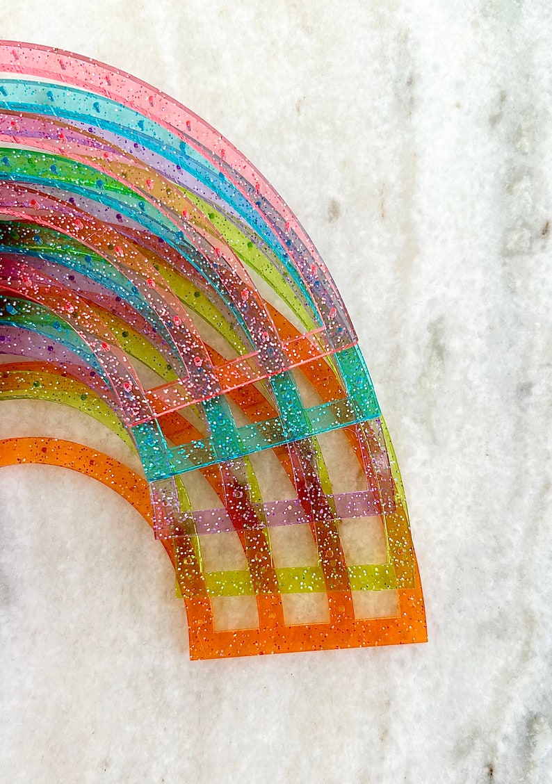 Pu&ograve; includere: Un set di righelli in plastica arcobaleno con glitter incorporati nella plastica. I righelli sono disposti a forma di semicerchio, con il righello pi&ugrave; grande in basso e il pi&ugrave; piccolo in alto.