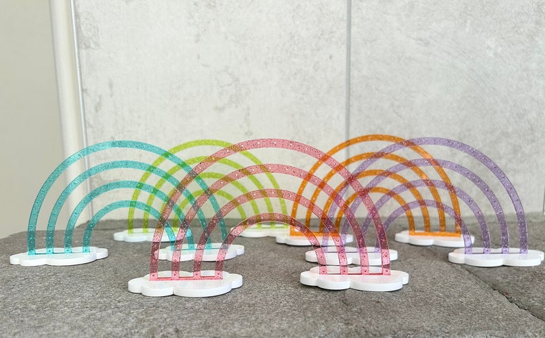 Pu&ograve; includere: Un set di sette archi in plastica arcobaleno, ognuno con una base a forma di nuvola. Gli archi sono disposti in fila, con l'arco pi&ugrave; grande dietro e l'arco pi&ugrave; piccolo davanti. Gli archi sono realizzati in plastica trasparente con una finitura scintillante.