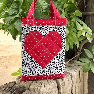 May include: A red and white quilted tote bag with a large heart design. The heart is made of red fabric with white polka dots and is surrounded by a black and white dalmatian print fabric.