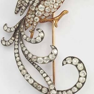 Può includere: Un broche in argento e oro a forma di pavone con una lunga coda di diamanti. La testa del pavone è adornata con pietre preziose verdi e rosse.