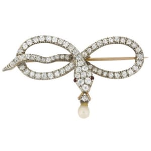 May include: A silver and gold snake brooch with a pearl dangling from its mouth. The snake is set with diamonds and has a ruby eye.