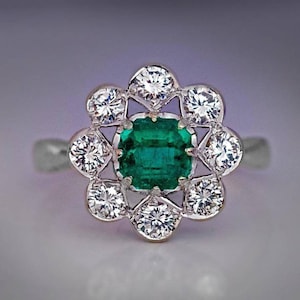May include: A silver ring with a green emerald gemstone surrounded by a halo of smaller diamonds.