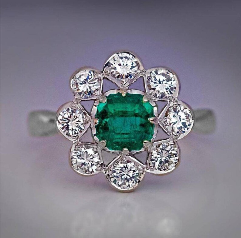 May include: A silver ring with a green emerald gemstone surrounded by a halo of smaller diamonds.