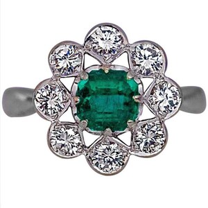 May include: A silver ring with a green emerald gemstone surrounded by a halo of smaller diamonds.