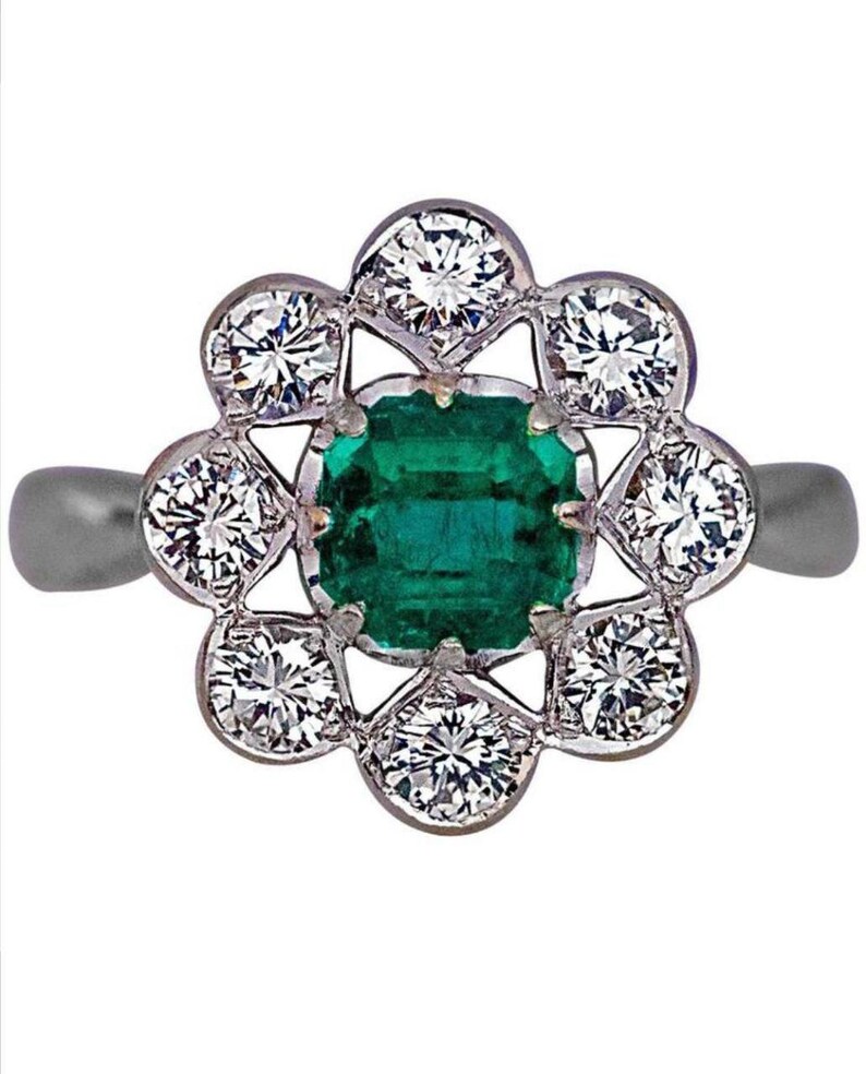 May include: A silver ring with a green emerald gemstone surrounded by a halo of smaller diamonds.