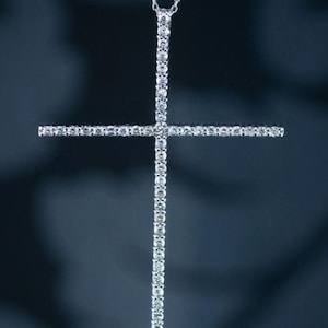 May include: A silver cross pendant necklace with a diamond-encrusted design. The cross is set against a dark background.