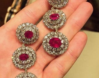 Puede incluir: Un par de pendientes largos y colgantes con múltiples acentos de rubí y diamantes. Cada pendiente presenta tres rubíes redondos engastados en bisel rodeados por un halo de diamantes más pequeños.