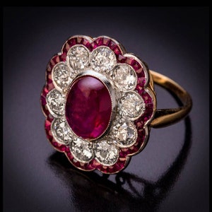 May include: A gold ring with a large red ruby cabochon surrounded by a halo of smaller diamonds and red rubies.
