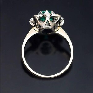 May include: A gold ring with a large emerald gemstone surrounded by smaller diamonds. The ring is set in a white metal setting.